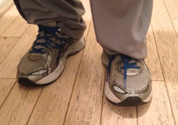 picture of a person wearing gray sweatpants and gray running shoes with blue laces on a white washed wood floor 