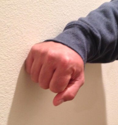 picture of a man's fist sideways against an off white wall to demonstrate how deaf people can get one another's attention by banging on the wall. 