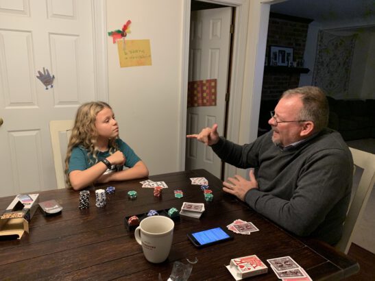 a CODA and her Deaf dad sit at a kitchen table playing a card game while signing