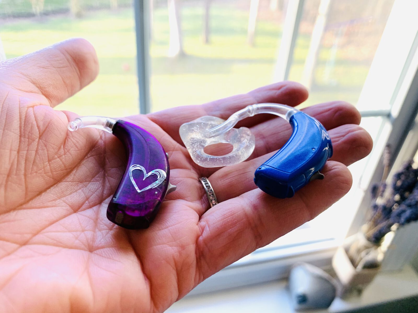 what to expect from hearing aids. purple and blue hearing aids resting on open hand