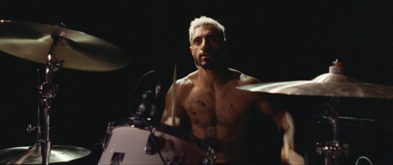 Riz Ahmed as Ruben in Sound of Metal drumming behind a drum kit. He is not wearing a shirt.