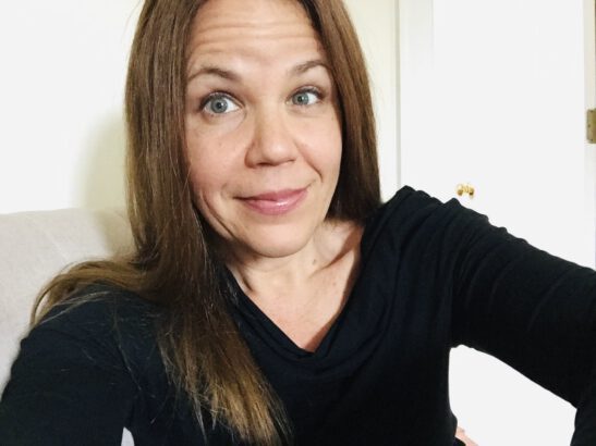 Jen Leora selfie - she is wearing a black v-neck long sleeve shirt with long brown straight hair.