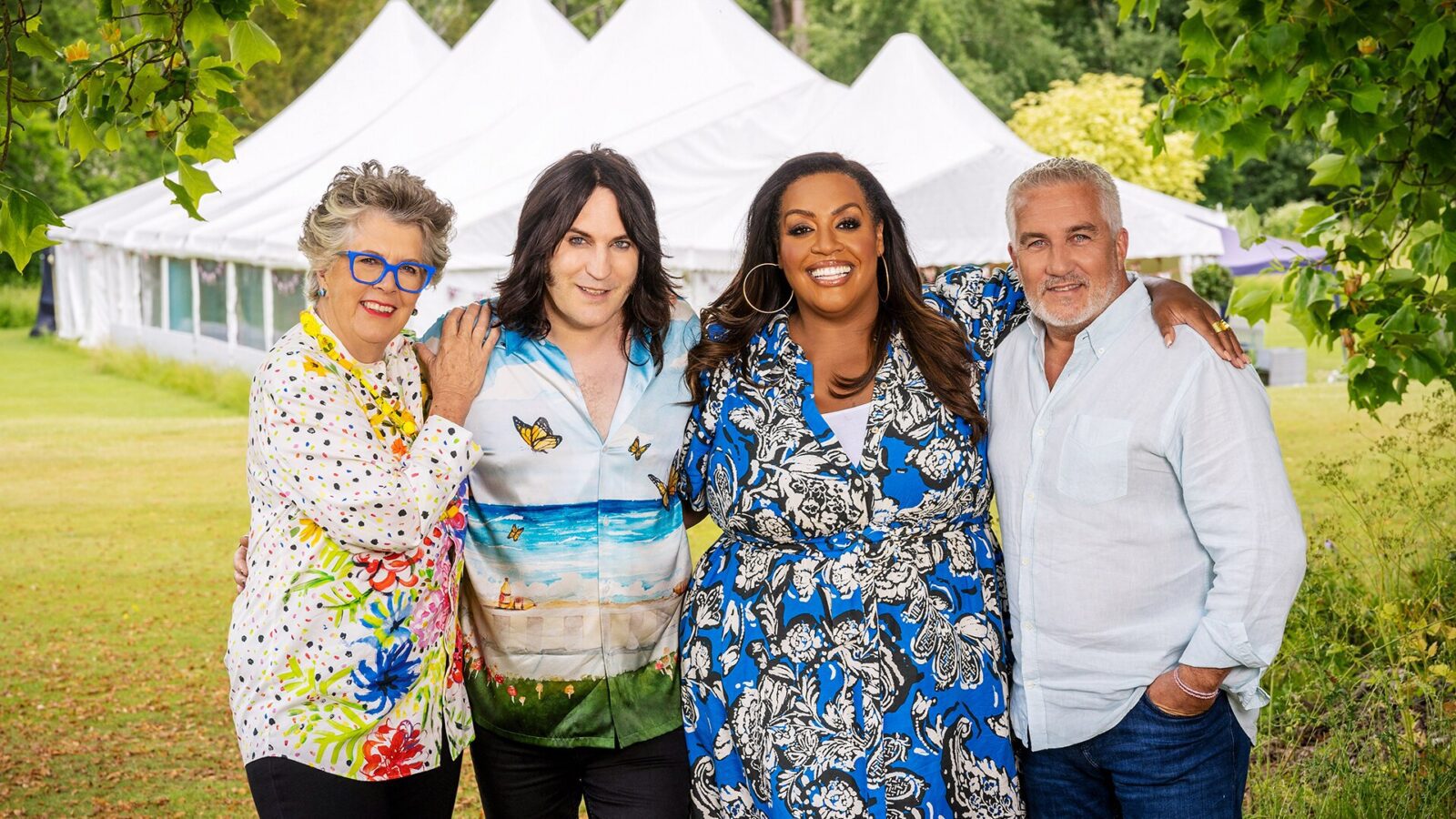 GBBO gets a Deaf baker - 4 hosts of the Great British Bake Off standing close together smiling at the camera in front of a white tent in the countryside.