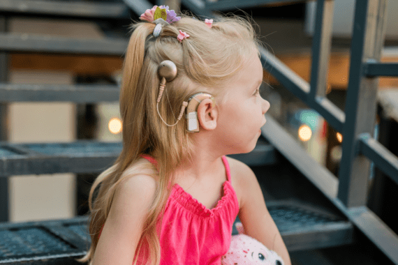 Child wearing a cochlear implant processor behind the ear with a circular external transmitter on her head